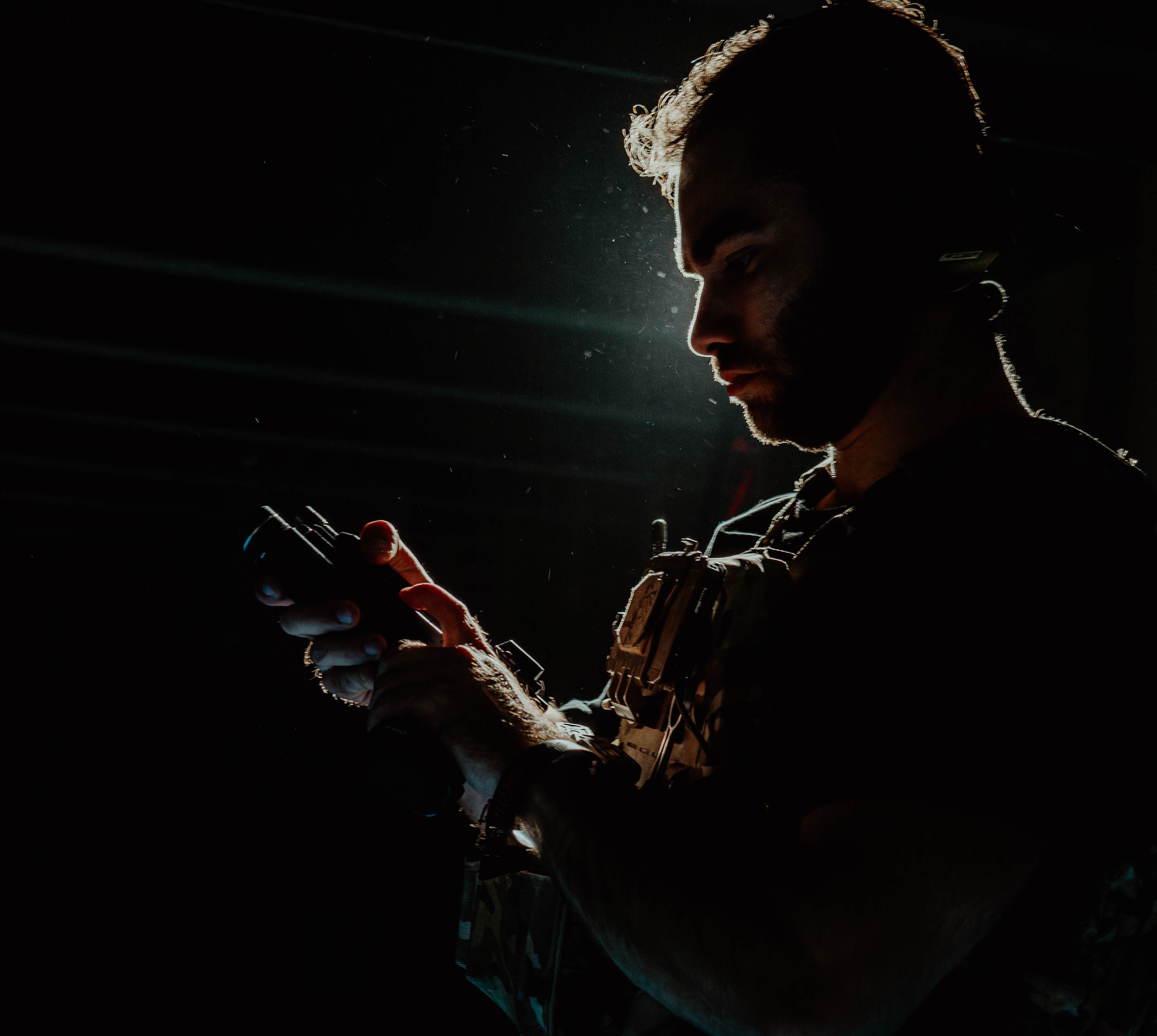 Tactical operator loading weapon while wearing PGL Armor plate carrier in dark environment